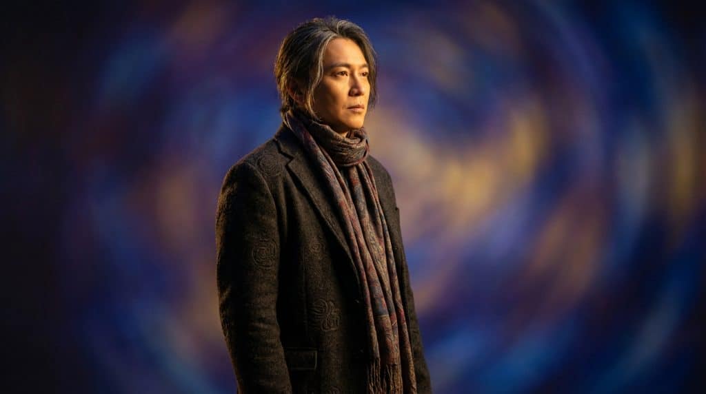 A man with a pensive expression, graying hair, in a patterned scarf and dark textured jacket, against a vibrant, swirling abstract background.