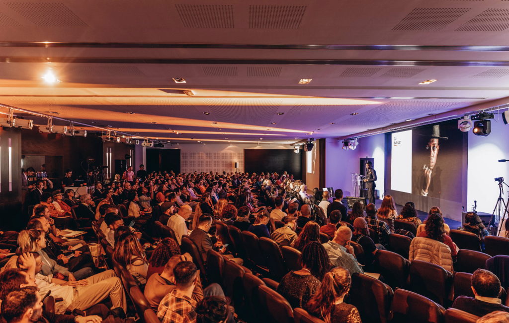 Salle de conférence comble avec conférencier et grand écran