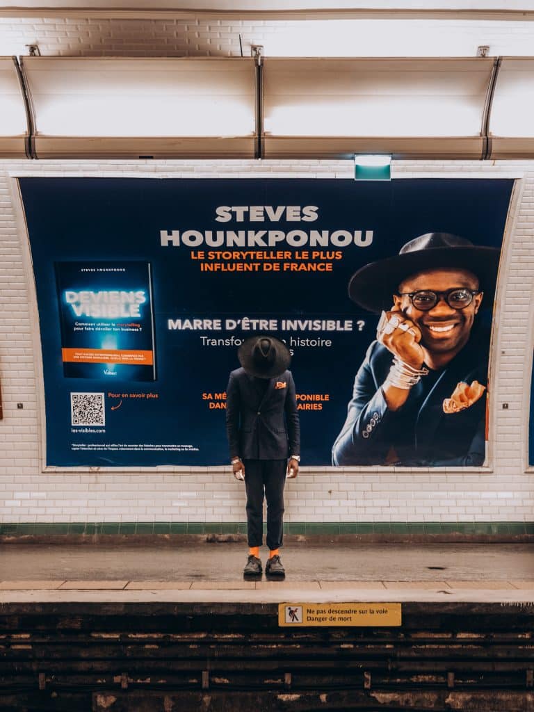 Homme devant affiche publicitaire Steves Hounkponou dans le métro parisien